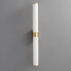A pale white alabaster tube wall light with a brass band, on a grey wall, with little visible veining, from Clérachic.