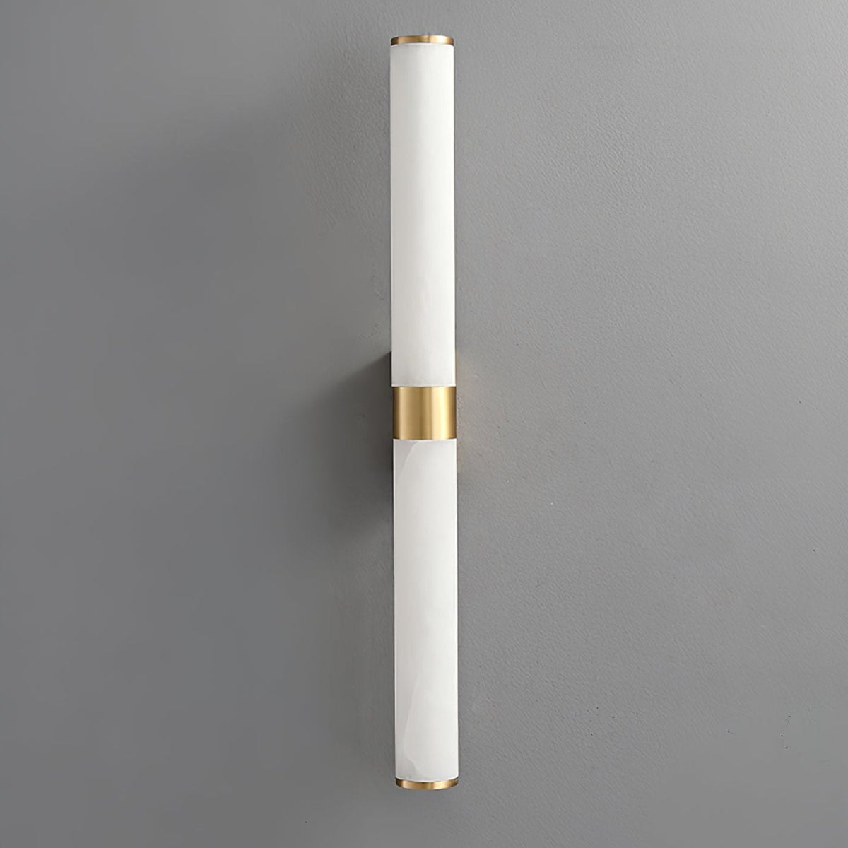 A pale white alabaster tube wall light with a brass band, on a grey wall, with little visible veining, from Clérachic.