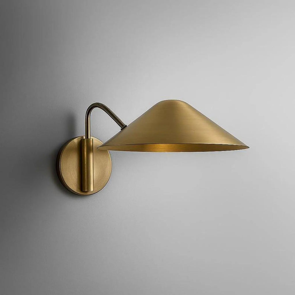 Clérachic brass wall light with a broad cone shade on a curved arm and a round wall plate, studio view