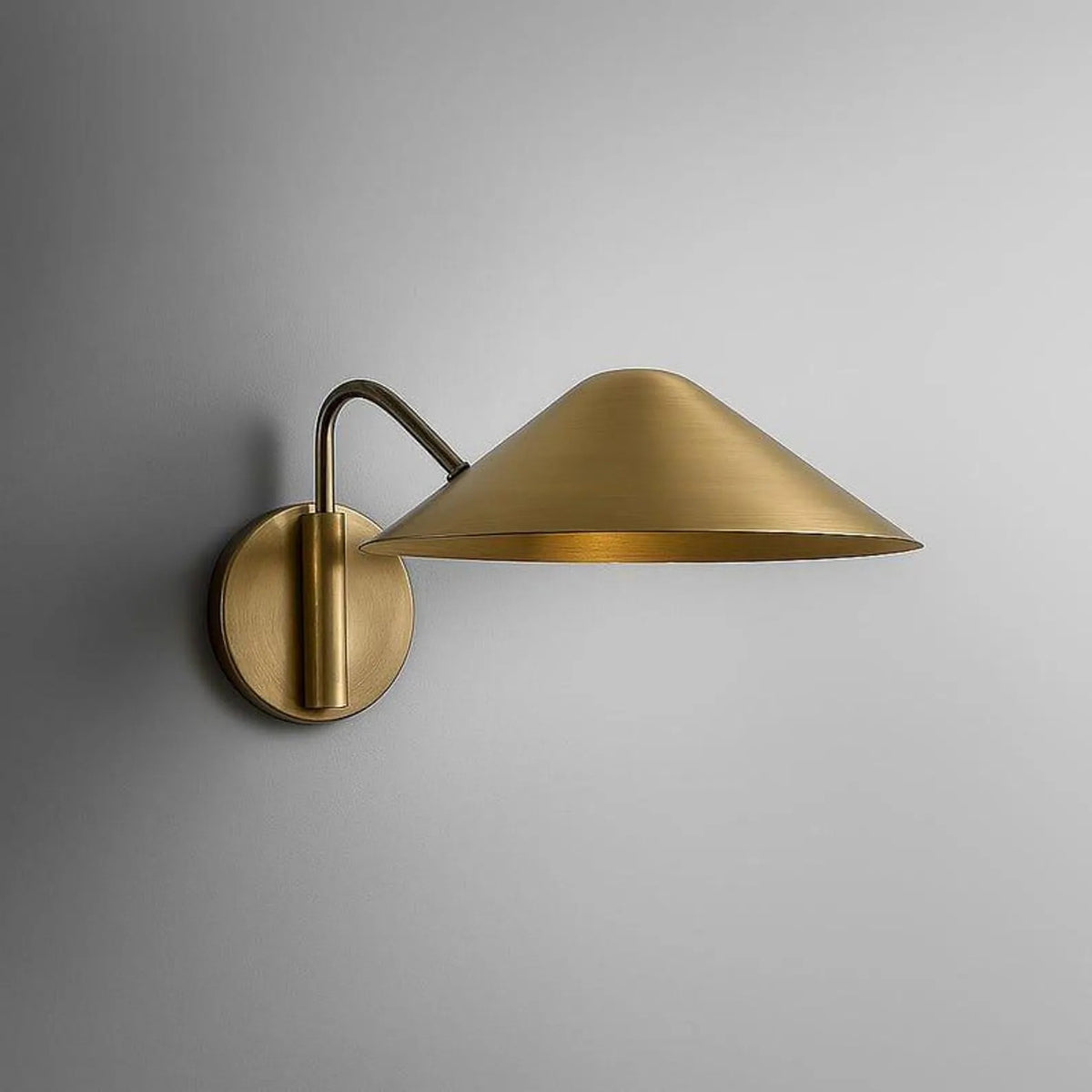 Clérachic brass wall light with a broad cone shade on a curved arm and a round wall plate, studio view