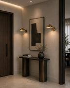 Pair of Clérachic brass cone-shade wall lights glowing either side of framed art above a dark console in a hallway