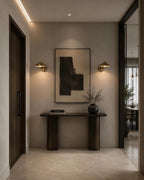 Two Clérachic brass cone-shade wall lights lighting a hallway console and abstract artwork, seen at an angle