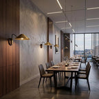 Row of Clérachic brass cone-shade wall lights along a restaurant wall above a long dining table