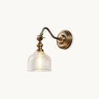 Antique brass wall light with a curved swan-neck arm and a ribbed clear glass shade, a Clérachic sconce on a plain backdrop.