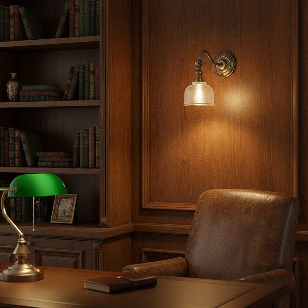 Warm light from a Clérachic brass wall light on a wood-panelled wall, near a bookcase and a green-shaded desk lamp.