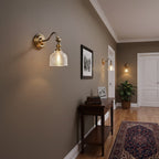A Clérachic brass wall light with a curved arm in a hallway with a framed photograph, more sconces further along and a patterned runner.