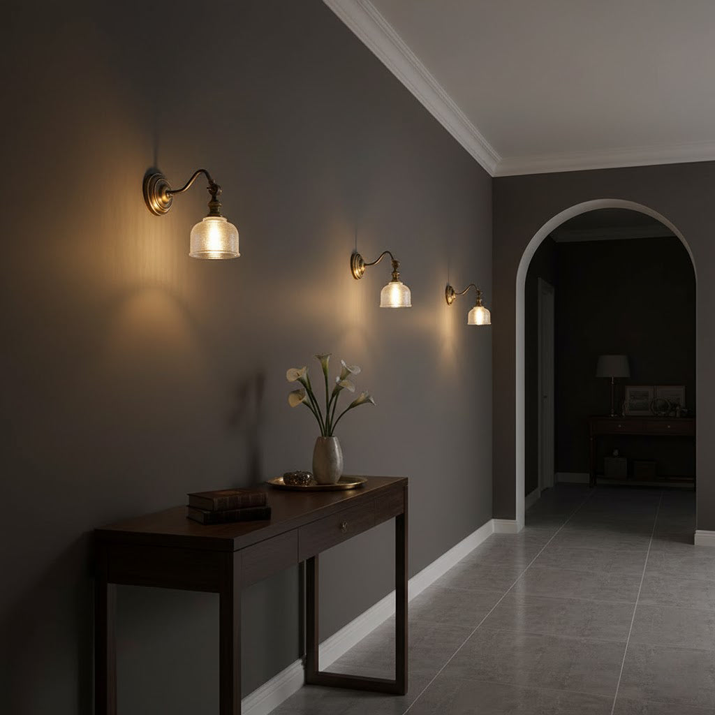 Three Clérachic brass wall lights run along a dark grey wall, above a narrow console table with a vase of flowers.