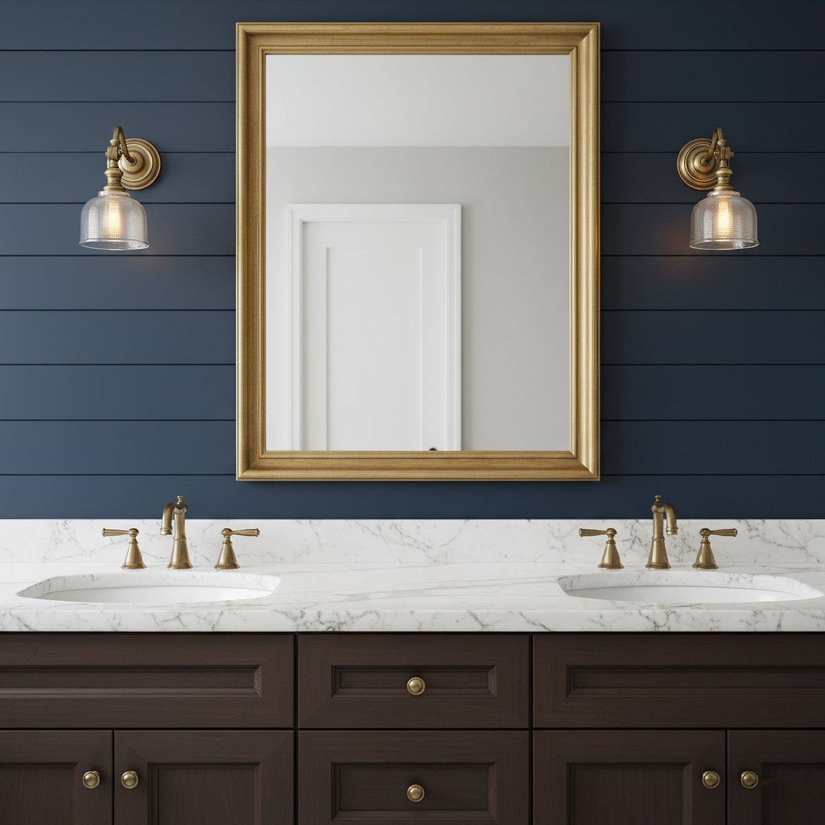 A pair of Clérachic wall lights with glass shades flank a gold-framed mirror on a navy boarded wall, above a double marble vanity.
