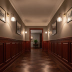 Clérachic brass wall lights with glass shades line both sides of a long hallway with dark wood panelling and a parquet floor.