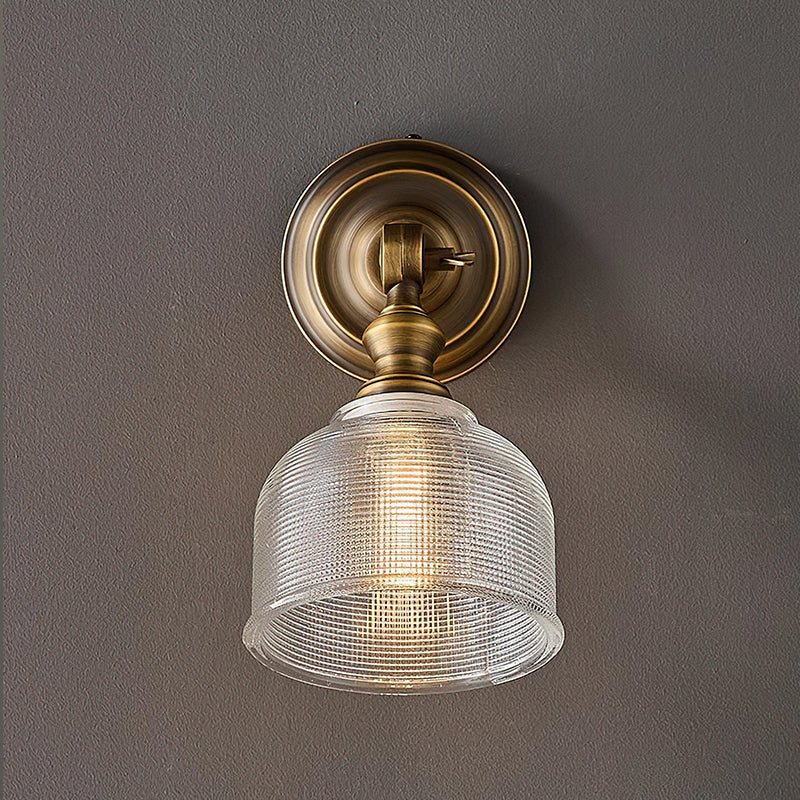 Close view of the ribbed glass shade, brass neck and round backplate of this Clérachic wall light, lit on a grey wall.