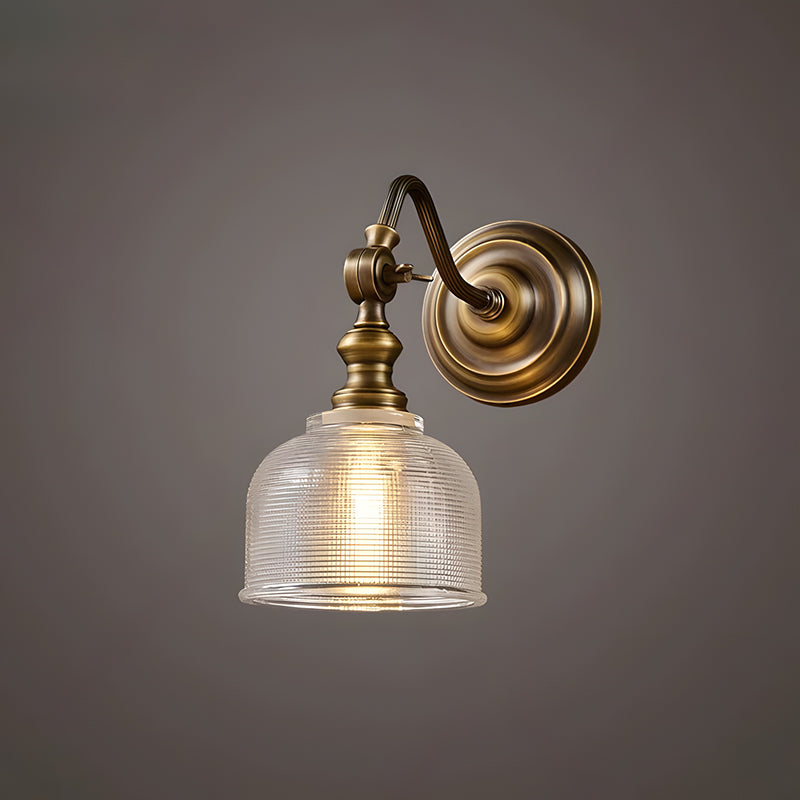 A Clérachic antique brass wall light with a swan-neck arm and a ribbed glass shade, lit warm on a dark grey backdrop.