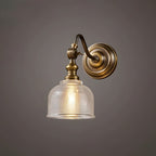 A Clérachic antique brass wall light with a swan-neck arm and a ribbed glass shade, lit warm on a dark grey backdrop.