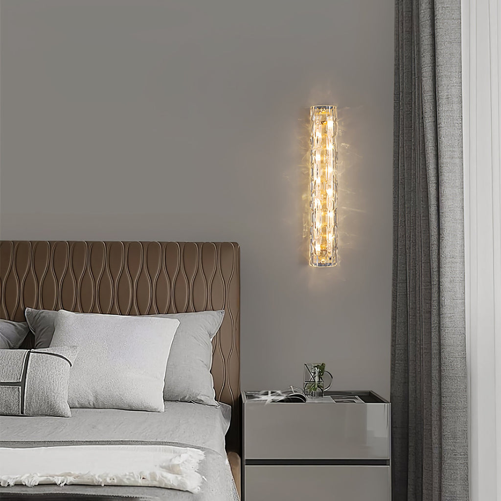 Slim Clérachic wall light lit beside a grey curtain, above a bedside cabinet and a bed with a tan quilted headboard.