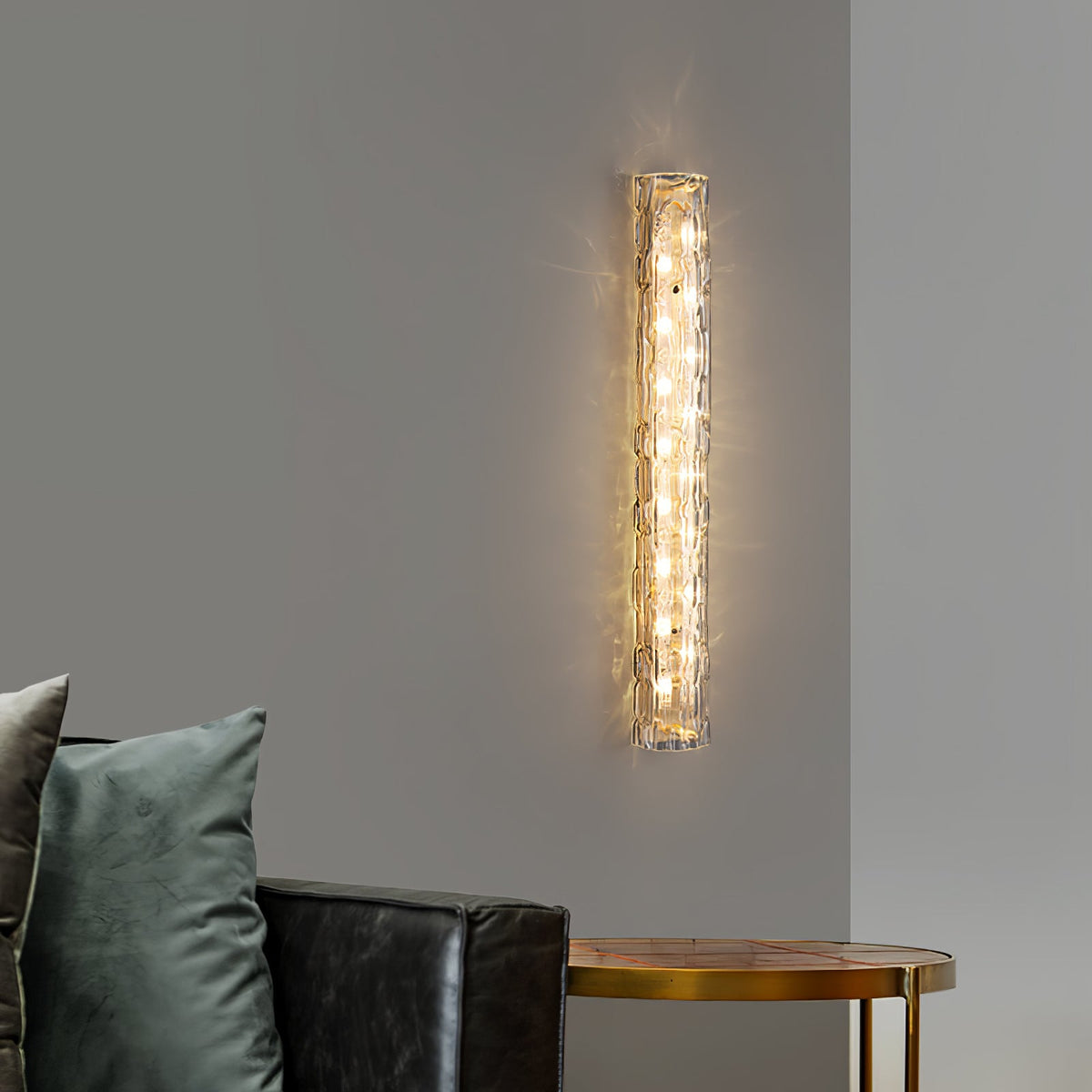 Vertical Clérachic sconce lit on a grey wall, with a green cushion and a dark leather sofa below.