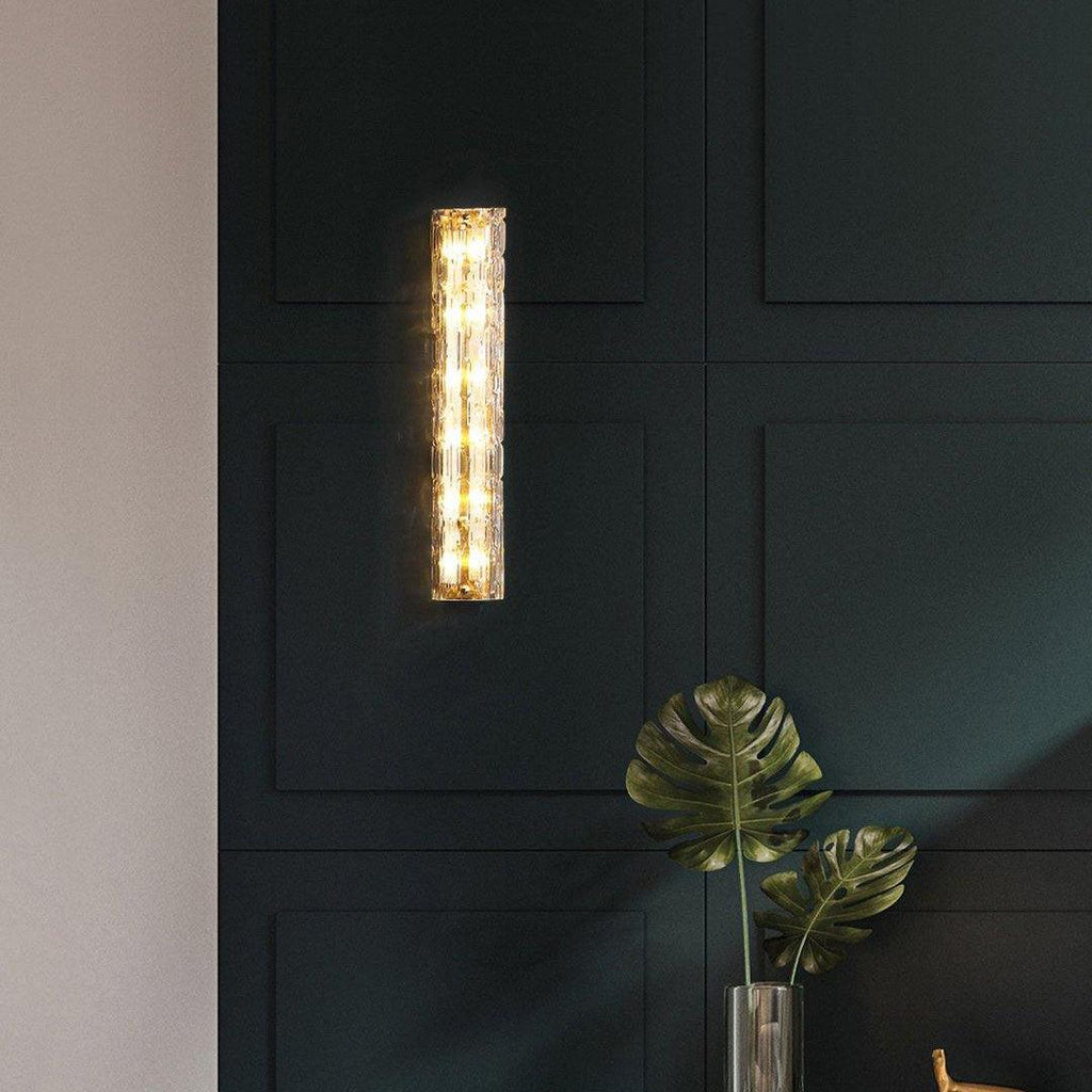 Clérachic wall light on a deep green panelled wall, with the leaves of a large green plant at the bottom of the frame.
