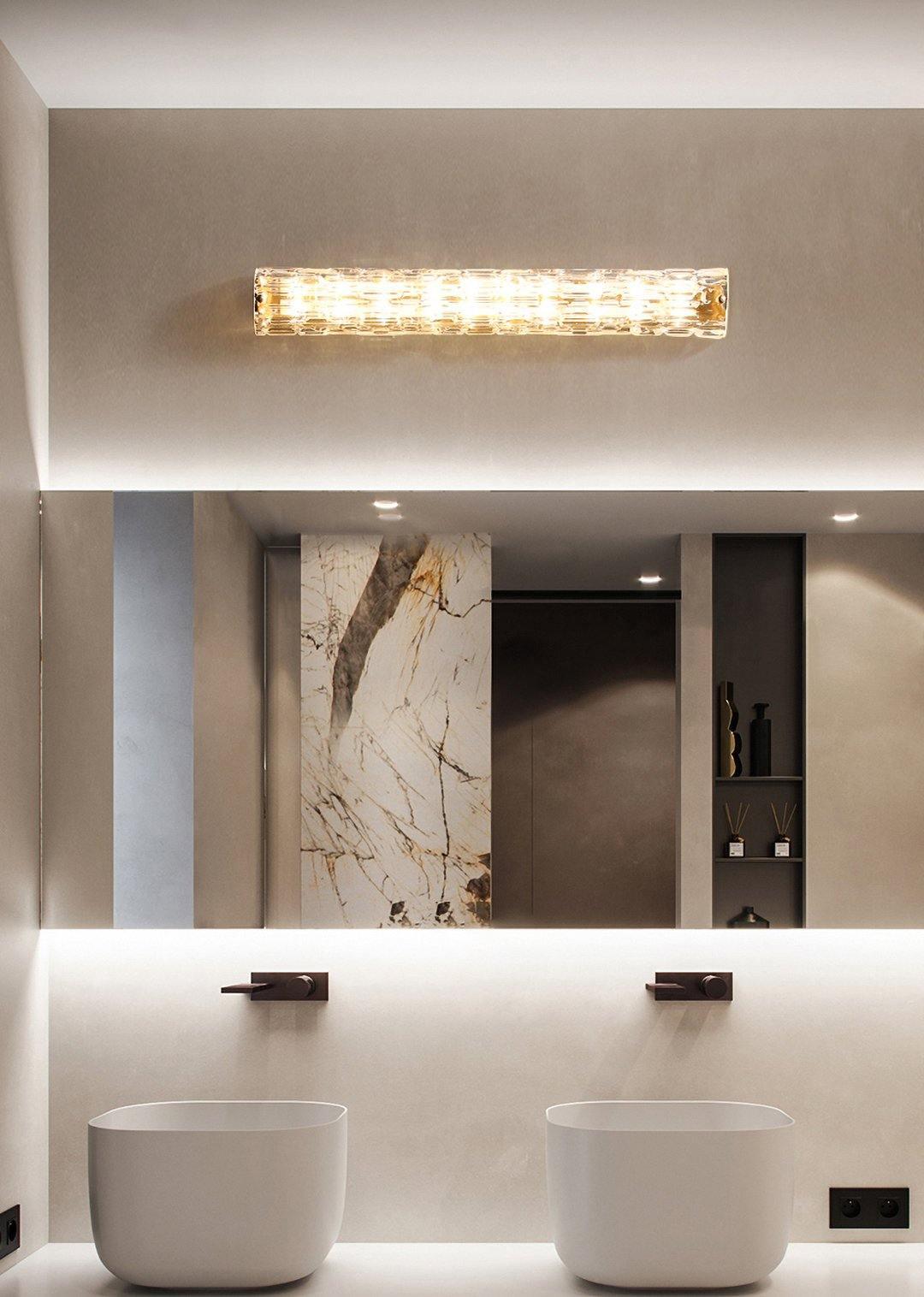 A Clérachic glass wall light mounted horizontally above a double bathroom vanity, with two round basins and a marble panel below.