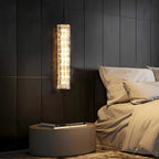 Lit Clérachic wall light on dark wood panelling, with a round bedside table and a bed in rumpled beige linen.