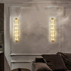Two Clérachic glass wall lights lit on a pale wall with ornate white mouldings, above a sofa with dark cushions.