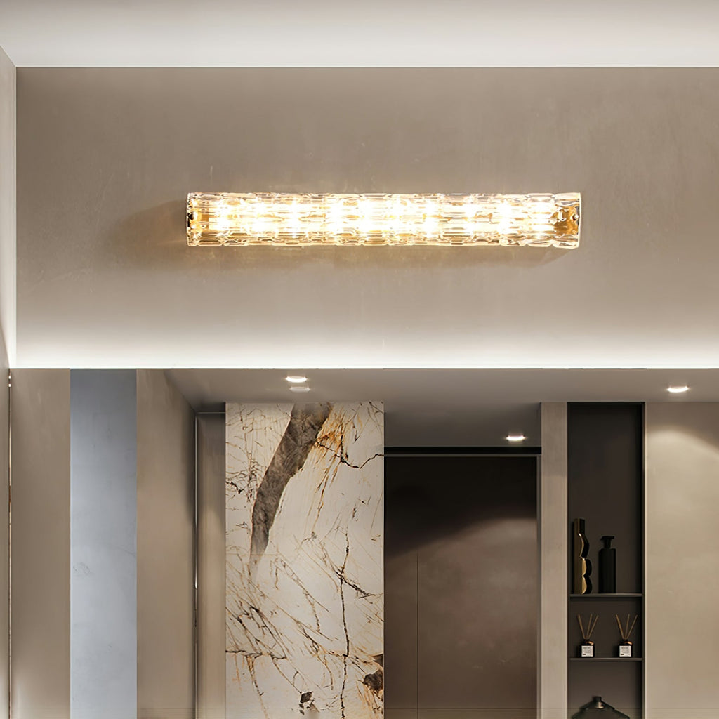 Horizontal Clérachic glass wall light lit above a bathroom mirror, with a marble-veined panel and shelving in the room below.
