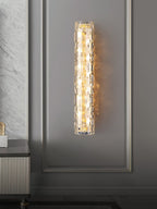 A Clérachic glass wall light lit on a panelled grey wall, with a marble-effect wall and a fluted cabinet to the left.