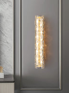 A Clérachic wall light lit in the centre of a panelled grey wall, with marble-effect stone at the left edge.