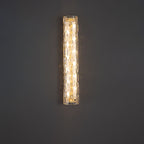 Clérachic glass wall light lit against a plain dark grey wall, its warm bulbs showing through the textured shade.
