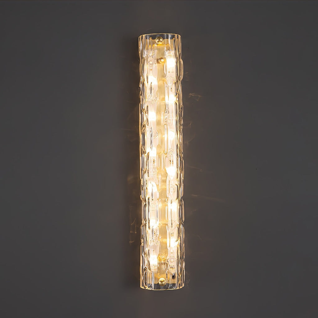 Close front view of a lit Clérachic wall light on a dark grey wall, with rippled clear glass and gold fittings.