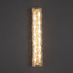 Close front view of a lit Clérachic wall light on a dark grey wall, with rippled clear glass and gold fittings.