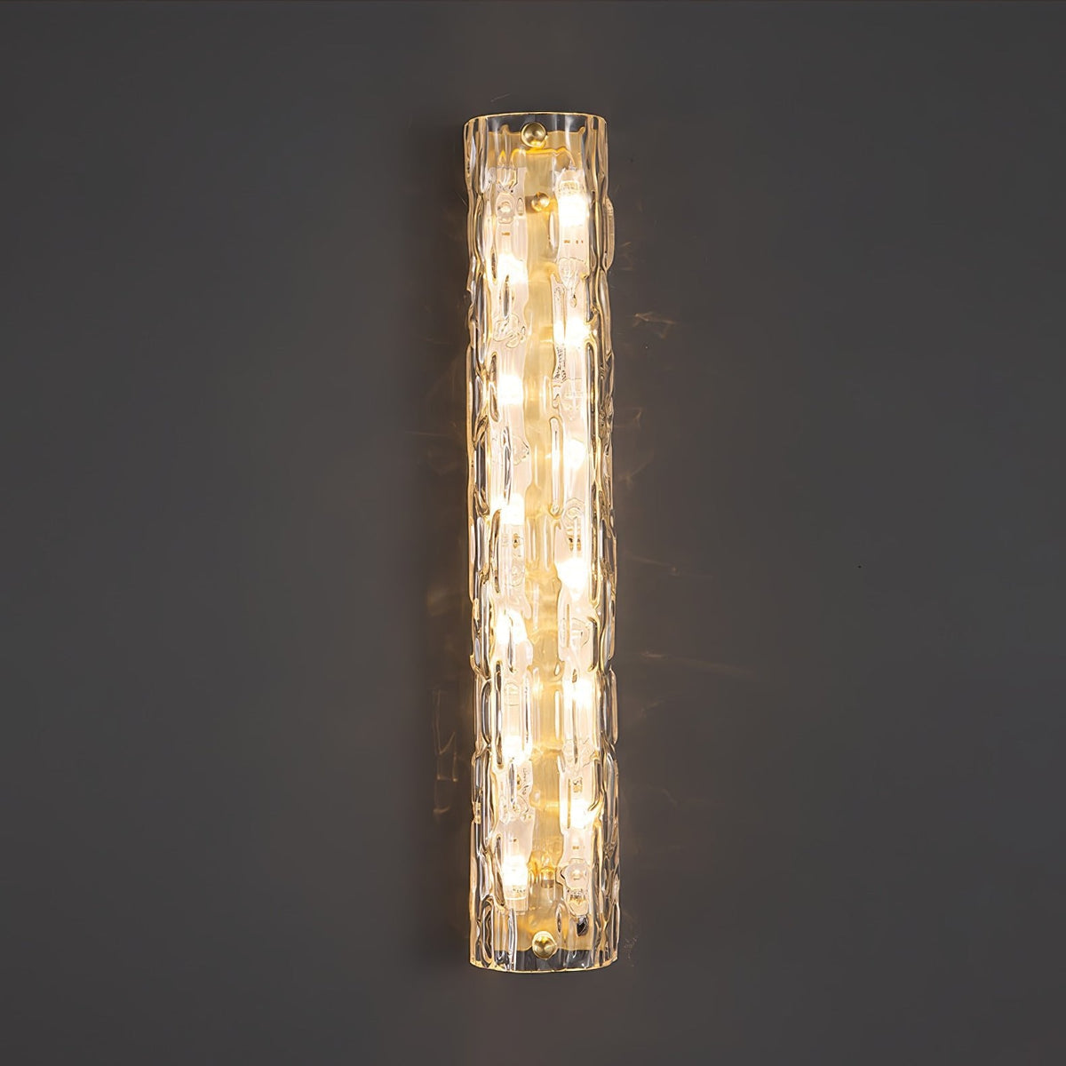 Close front view of a lit Clérachic wall light on a dark grey wall, with rippled clear glass and gold fittings.
