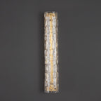 Unlit Clérachic wall light on a dark grey wall, showing clear rippled glass over a brushed gold backplate.