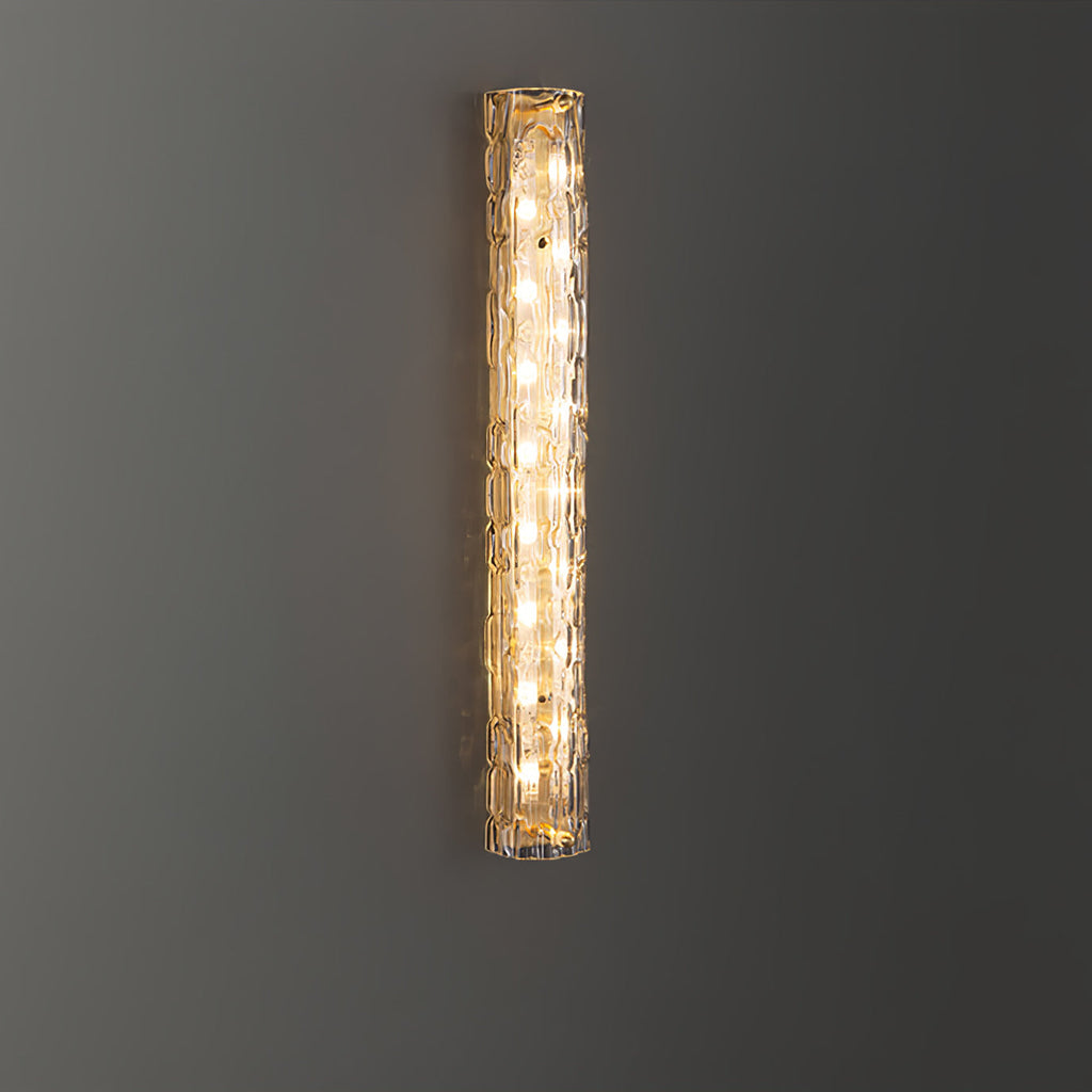 Clérachic wall light lit against a dark grey wall, a column of bulbs glowing behind the textured glass.