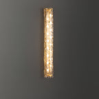 Clérachic wall light lit against a dark grey wall, a column of bulbs glowing behind the textured glass.