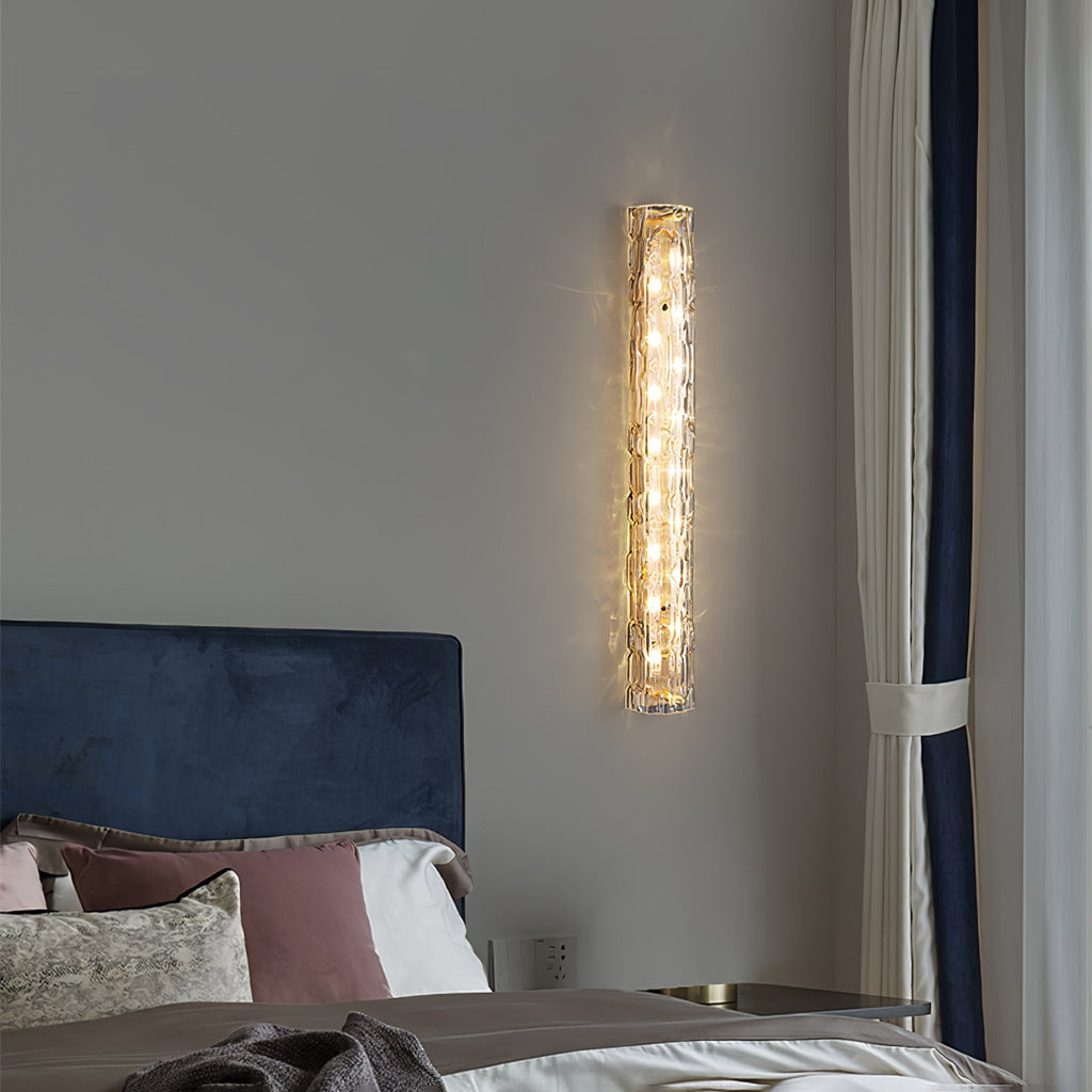 Clérachic wall light lit on a grey wall, with a blue velvet headboard and a curtain with navy edging below.