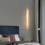 Clérachic wall light lit on a grey wall, with a blue velvet headboard and a curtain with navy edging below.