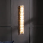 Clérachic glass wall light lit on dark panelling, with a blue cushion at the bottom edge of the frame.