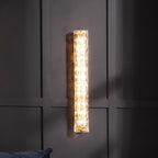 Clérachic wall light lit on a dark panelled wall, with the edge of a blue cushion at the bottom.