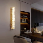 A Clérachic wall light lit above a leather desk chair, beside shelving with lit books and a bed beyond.