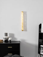 Clérachic wall light lit as a gold strip on a pale grey wall, with a black chest of drawers and a striped vase below.
