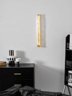 Clérachic wall light on a pale grey wall, only faintly glowing, above a black chest and a black-and-white striped vase.