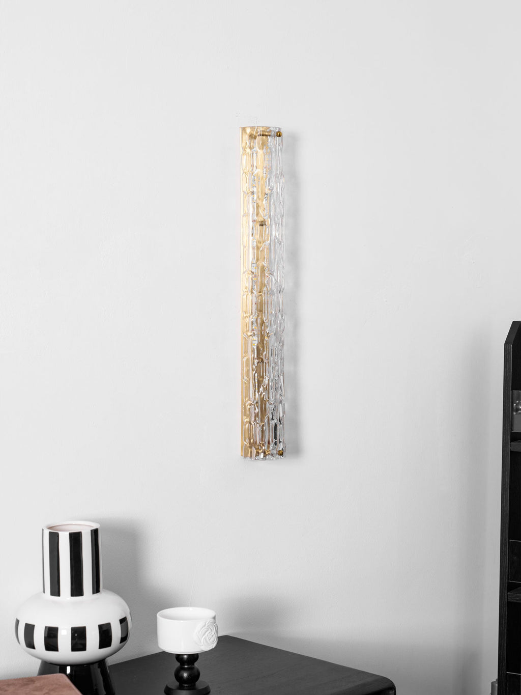Clérachic glass wall light with a gold backplate beside the edge of a dark chest and a striped vase.