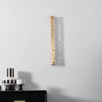 Clérachic wall light, unlit, on a pale wall above a black chest, with a striped vase and a shadow cast beside it.