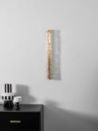 Smaller view of an unlit Clérachic wall light on a pale wall, above a black cabinet and a striped vase.