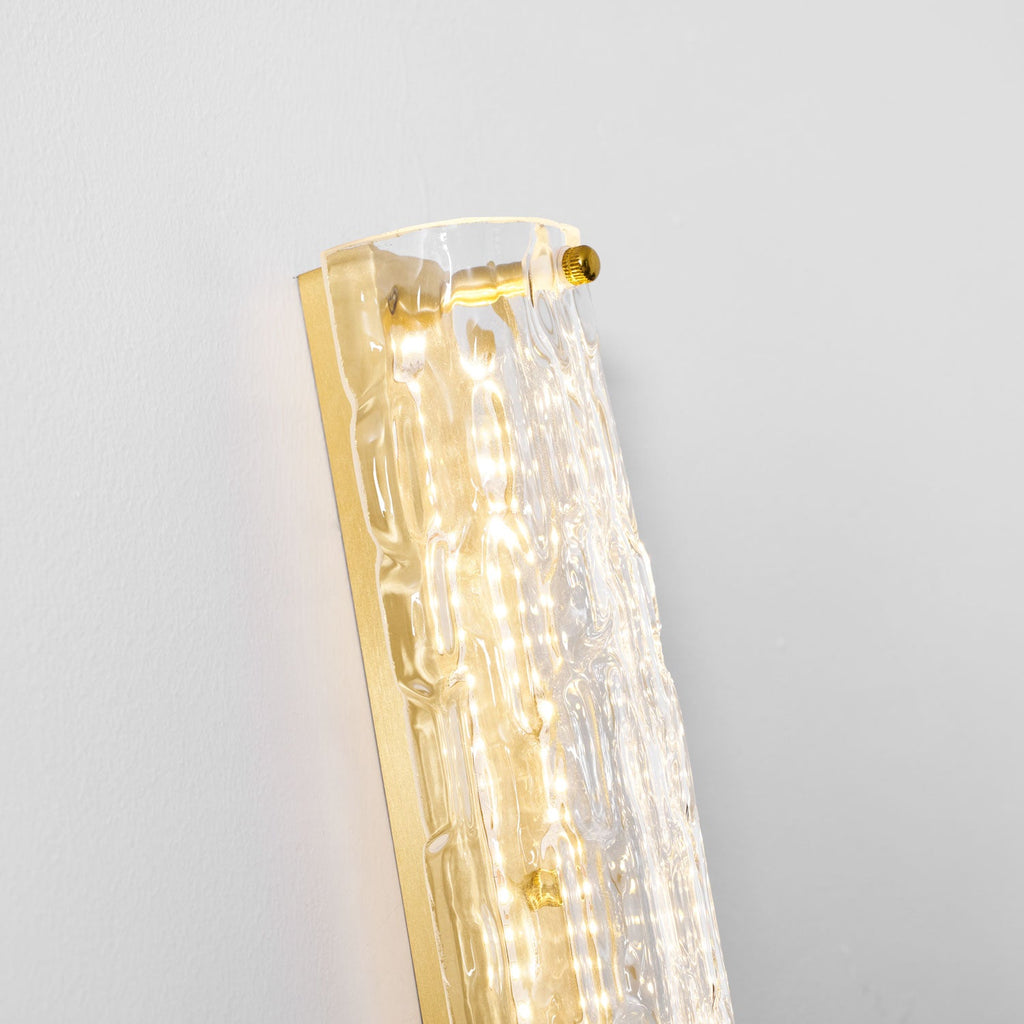 Close view of the top of this Clérachic wall light, with brass screws, gold backplate and rippled glass lit from inside.