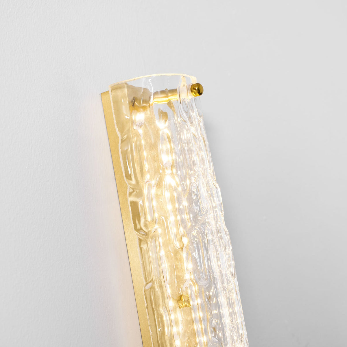Close view of the top of this Clérachic wall light, with brass screws, gold backplate and rippled glass lit from inside.