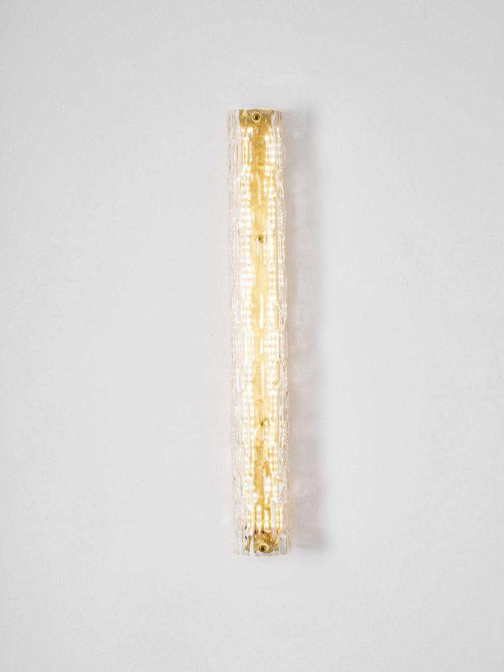 Lit Clérachic wall light on a pale wall, a warm column of LEDs showing through the rippled clear glass.