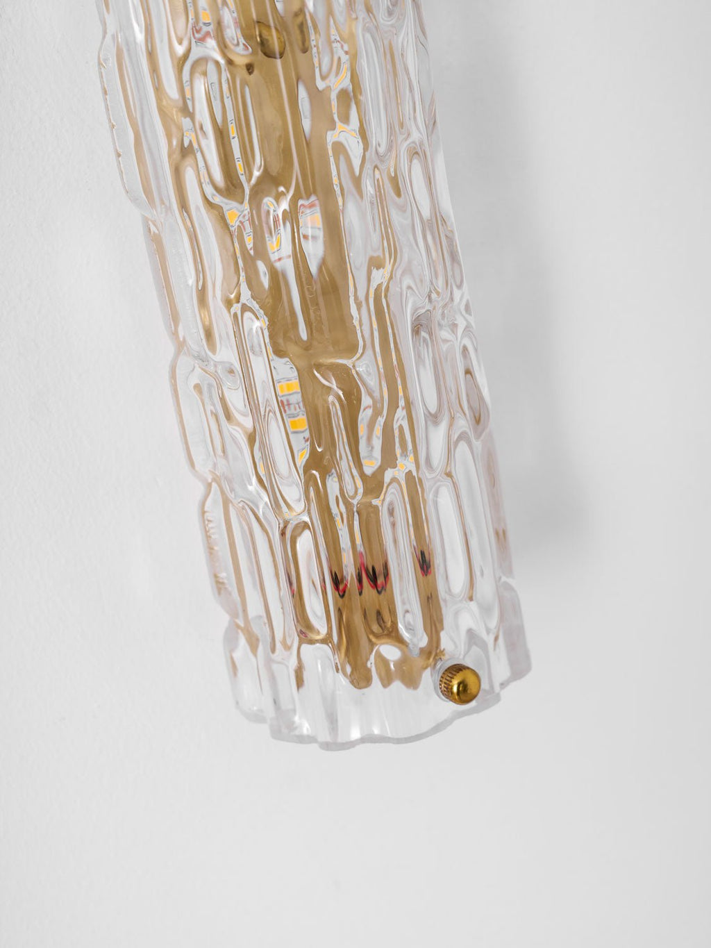 Close view of the bottom end of this Clérachic wall light, with rippled glass, gold backplate and a brass screw.