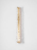 Unlit Clérachic wall light on a pale wall, its clear rippled glass wide over a gold backplate.