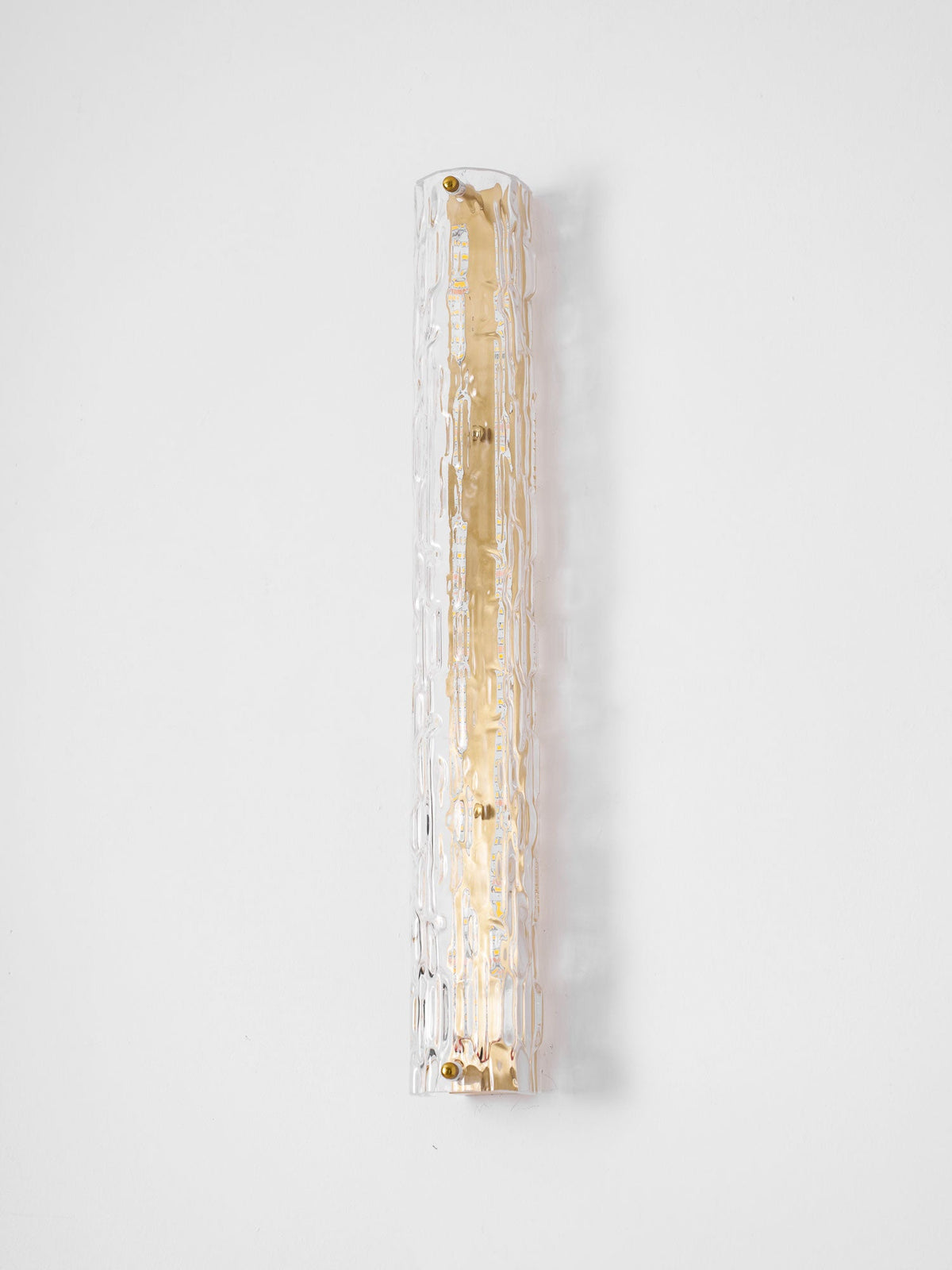 Unlit Clérachic wall light on a pale wall, its clear rippled glass wide over a gold backplate.