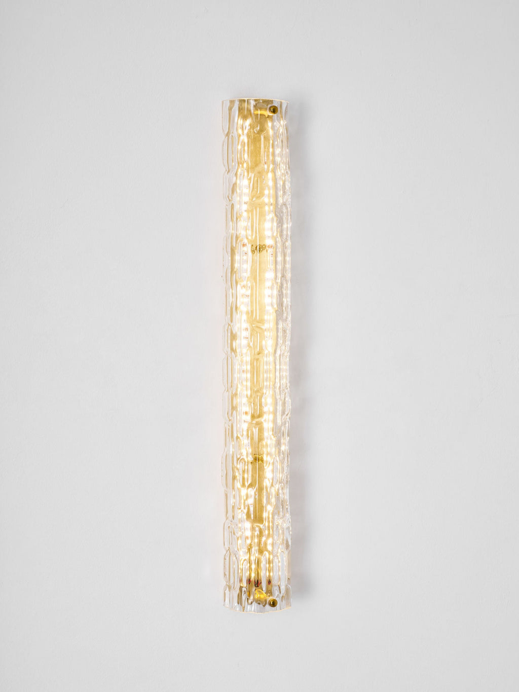 Clérachic wall light lit on a pale wall, a narrow column of warm light behind the textured glass.
