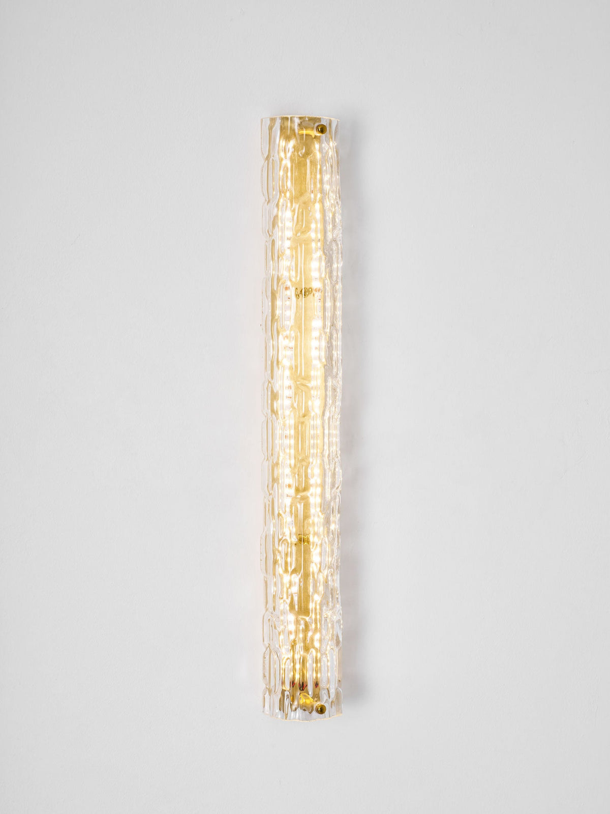 Clérachic wall light lit on a pale wall, a narrow column of warm light behind the textured glass.